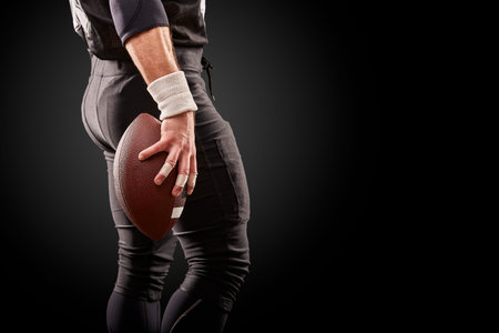 Mid section of American football player with ball against black, copy space, back viewの写真素材