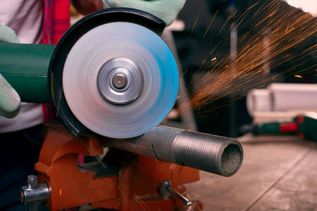 Gloved hands hold an angle grinder and cut the pipe, many sparks fly to the sidesの写真素材