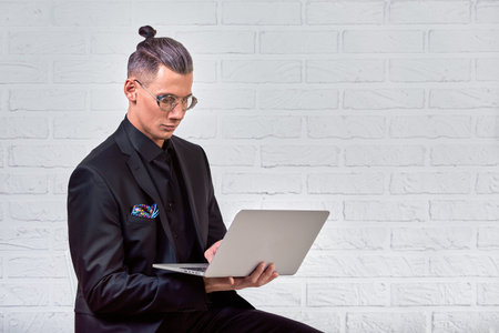 Handsome business man in glasses and suit holding laptop in hands and writing something. Side view....