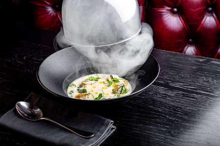 Cream soup is steaming in a black plate with on the black table. Photo for menuの写真素材
