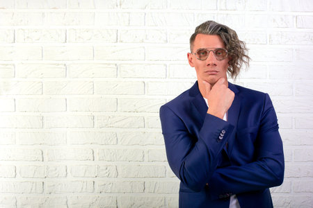 Portrait of stylish businessman with curly long hair in sunglasses smiling at the camera on white...