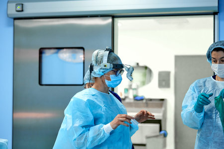 Assistant helps the surgeon put on latex gloves before the operation. A team of surgeons in the...