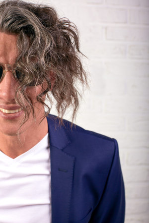 Portrait of stylish businessman with curly long hair in sunglasses smiling at the camera on white...