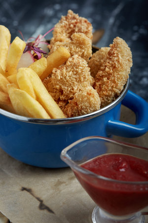 Lunch or snack - fried chicken strips and french fries in a metal pan with tomato sauce. Craft paper...