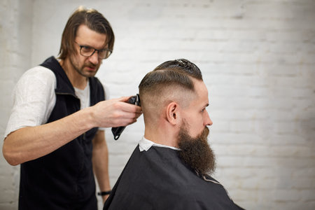 Brutal guy in modern Barber Shop. Hairdresser makes hairstyle a man with a long beard. Master...