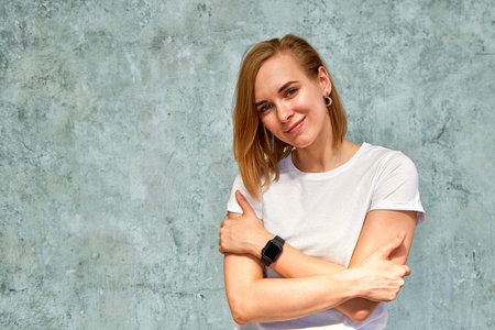 portrait of a beautiful, embarrassed girl on a background of gray wall in a white t-shirt
