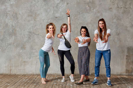 group of young girls are posing against the wall smiling and showing gestures with their hands. Gray background, save space.の写真素材
