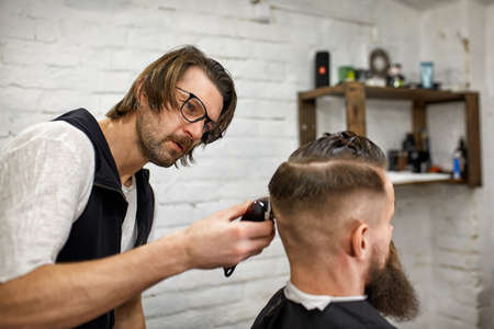 Stylish barber cuts a brutal man with a thick beard.の写真素材