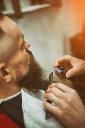 Master Barber does hairstyle and styling. Concept Barbershop. Beard styling and cut. styling of black beard. So trendy and stylish. Advertising and barber shop concept.の写真素材
