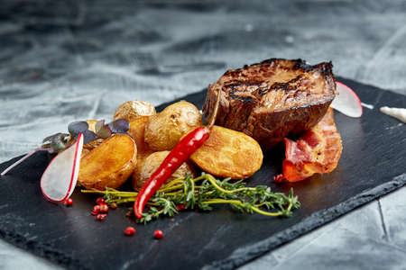 Beef steak served with baked potatoes and vegetables,black background, close-up. concept food.の写真素材