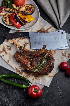 Tomahawk steak with vegetables and a knife on the table. Grilled meat with grilled vegetables and...