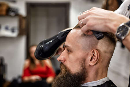 Master cuts hair and beard of men in the barbershop, hairdresser makes hairstyle for a young man.の写真素材