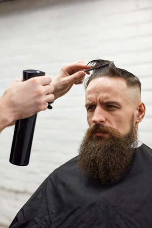 Brutal guy in modern Barber Shop. Hairdresser makes hairstyle a man with a long beard. Master hairdresser does hairstyle with hair clipperの写真素材