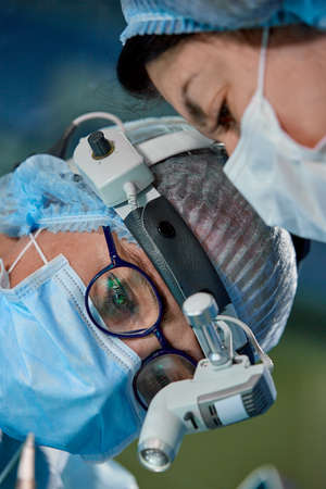 Surgeon performing cosmetic surgery in hospital operating room. Surgeon in mask wearing loupes during medical procadure. Breast augmentationの写真素材