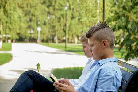 Two happy teenage friends using on mobile phone while relaxing in the park. Problems of modern youth, social networks, life online.の写真素材