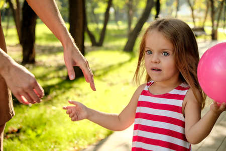 Mom holds the hand of a little girl with a balloon in the park. Close-up handshake. Happy family, mom daughter.の写真素材