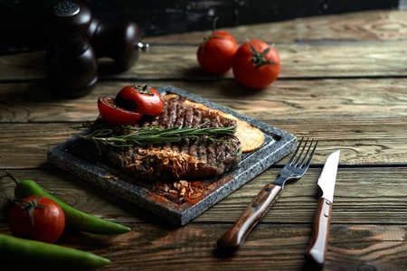 Grilled steak with knife and fork carved on black stone slate. Steak on a hot marble stone. Copy space, dark background, food fashion photo.の写真素材