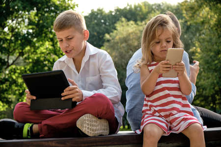 happy teenage friends using on mobile phone while relaxing in the park. Problems of modern youth, social networks, life online.の写真素材