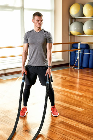 Fitness trainer man aggressive during shading with ropes in a bright fitness room for fitness. Sport...