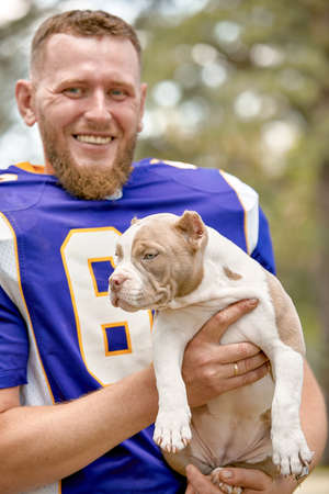 American football player with a dog posing on camera in a park. Copy space, sports banner. Concept american football, sport for the protection of animals.の写真素材