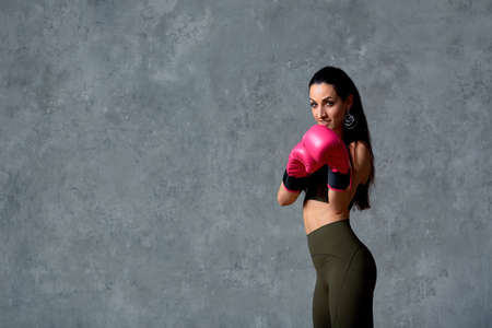 Beautiful athletic girl posing in pink boxing gloves on a gray background. Copy space. Concept sport, fight, goal achievement.の写真素材