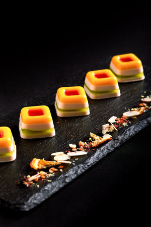 Colored marmalade, laid out in a beautiful line on a black plate. food background. Fusion food concept, low key, copy space.の写真素材