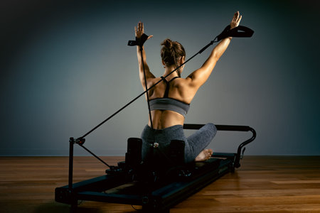Young girl doing pilates exercises with a reformer bed. Beautiful slim fitness trainer on reformer...