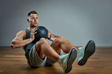 Strong man doing exercise with med ball. Photo of man perfect physique on grey background. Strength and motivation.の写真素材