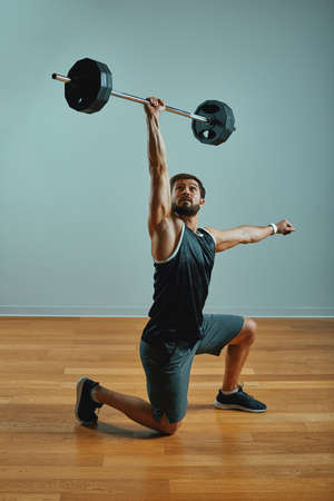 Portrait of super fit muscular young man working out in gym with barbell on gray background, copyspace.の写真素材