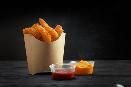 Fried tempura shrimps in paper to-go box. Served with sauces over black background. Copy space. Fast...