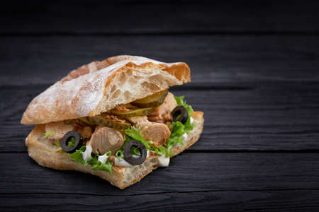 American fast food. Juicy tuna sandwich with cheese, salad and olives on a dark background. Club food.の写真素材
