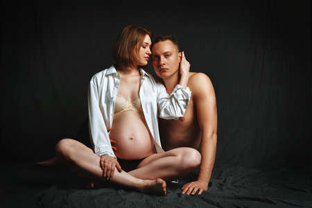 Pregnant couple posing for the camera on a brown background, low key. Fashion Pregnancy Concept. Copy space, brown background.の写真素材