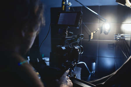 Video production backstage. Behind the scenes of creating video content, a professional team of cameramen with a director filming commercial ads. Video content creation, video creation industry. Low key, selective focus, film graineの写真素材