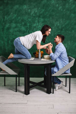 Young pregnant couple in the kitchen, cuddling, preparing food and rejoicing in anticipation of the baby. Concept new life, young family.の写真素材