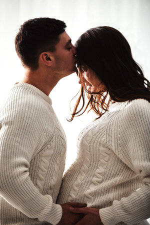 Close up portrait of expecting teenage couple laughing happily, embracing baby in belly together....