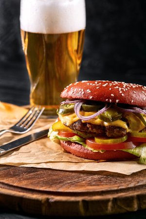 Delicious hot spicy black burger with chili pepper and glass of beer on cutting board on white wood...