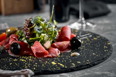 Beef carpaccio with arugula on a black plate, traditional Italian cuisine. Dark key, copy space,の写真素材