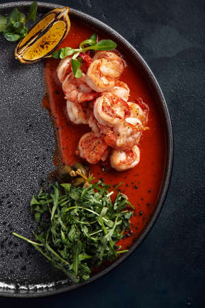 Grilled king tiger prawns with tomato sauce and arugula, beautiful serve from the chef, gray plate gray background. Bright beautiful flow of seafood, copies of space food photoの写真素材
