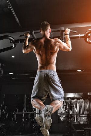 The athlete does pull-ups - chin in the gym, model with a sports body topless. Shot from the back,...