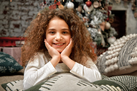Beautiful girl with curls against the background of Christmas decorations, lies on the floor and...