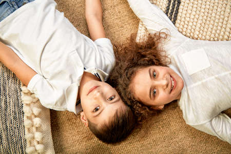Beautiful children a boy and a girl lie on the floor and look at the camera. The concept of happiness, friendship of children. Children are lying on the floor with their heads touching and smiling.の写真素材