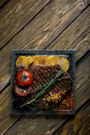 Grilled steak with knife and fork carved on black stone slate. Steak on a hot marble stone. Copy space, dark background, food fashion photo.の写真素材