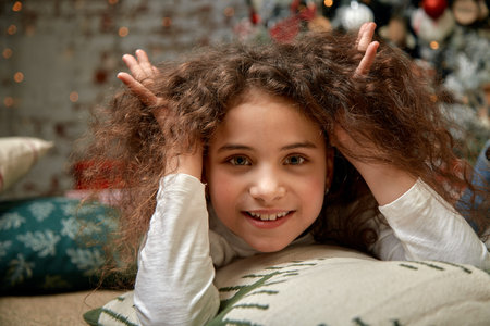 A beautiful girl with dark curly hair stands in the living room near the fireplace. New Years...