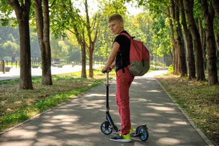 Boy on a scooter with a backpack in the park posing for the camera. Childrens entertainment in the...