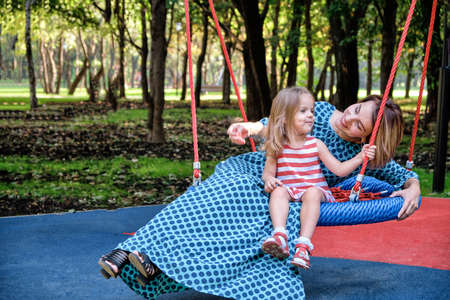 Mother and daughters on a swing in the park among the trees. Concept mom daughter, family happiness, relaxation in the cityの写真素材