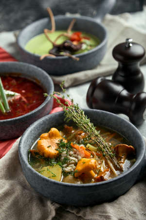 Gray plates with different soups on a gray background. Plate with asparagus soup with octopus, a plate of traditional borscht with sour cream, a plate with mushroom soup and standing on multi-colored linen napkins on a concrete marble gray background. Gray light texture background close-up top view. Beautiful table settingの写真素材