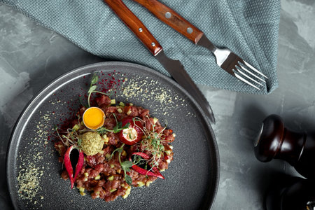 Beef tartare with egg yolk on a gray surface, top view, close-up.