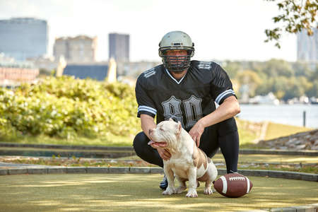 American football player with a dog posing on camera in a park. Copy space, sports banner. Concept american football, sport for the protection of animalsの写真素材
