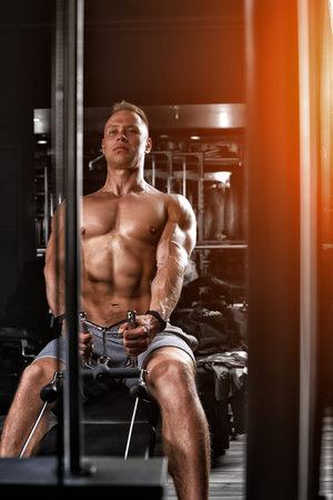 Handsome bodybuilder doing heavy weight exercise for the back on a simulator. Athletic body,...