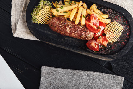 Kebab with french fries, chips and fresh tomatoes, served on a wooden plate. Food photo, traditional...